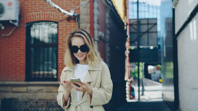 Eine Frau mit Sonnenbrille schaut auf der Straße auf ihr Handy