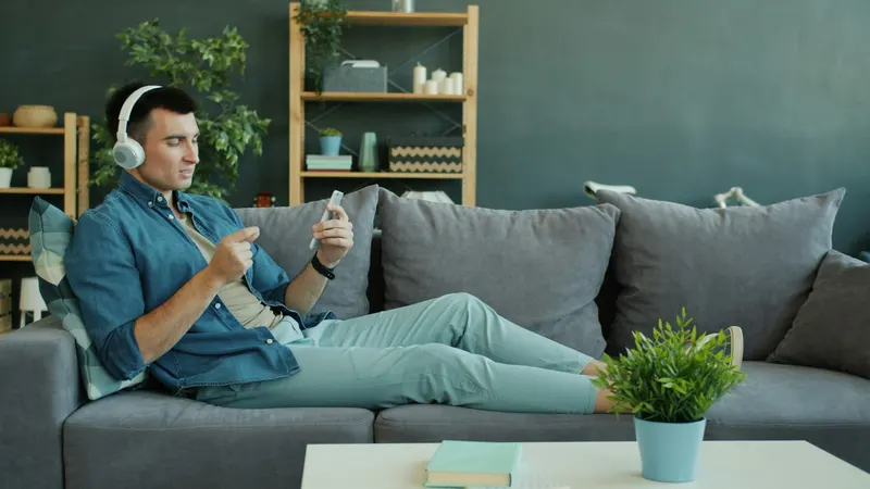 Ein Mann mit Kopfhörern schaut auf dem Sofa auf sein Handy
